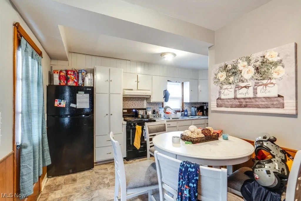 Kitchen featuring black appliances, white cabinets, light countertops, backsplash, and under cabinet range hood