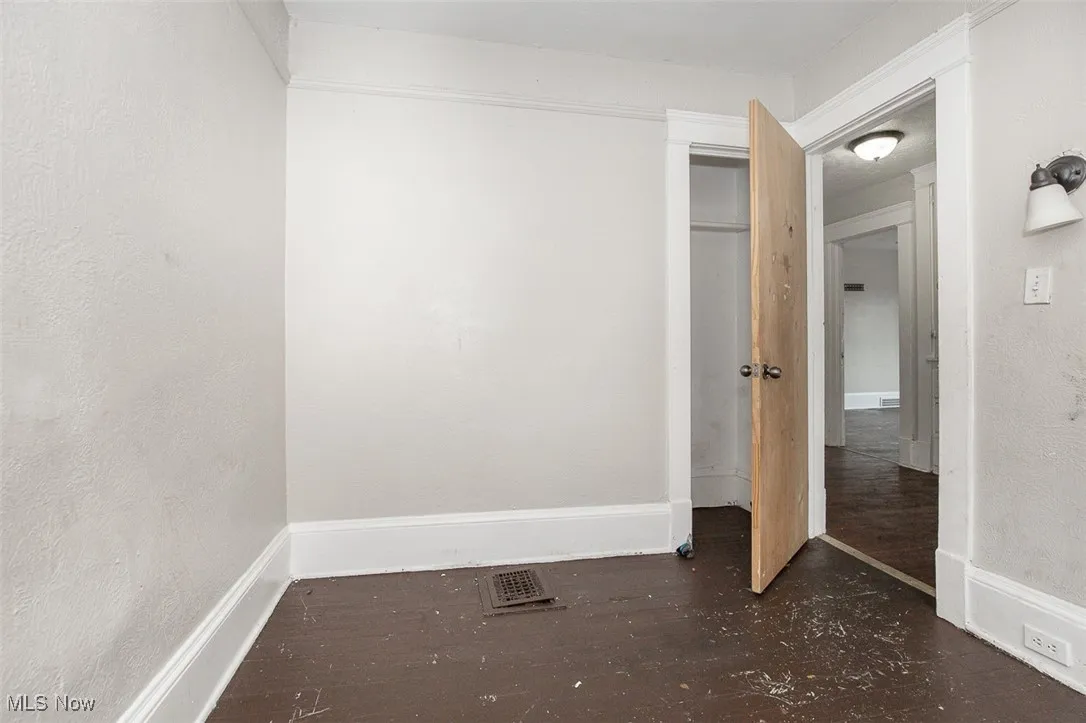 Unfurnished bedroom with a textured wall, dark wood-type flooring, and a closet