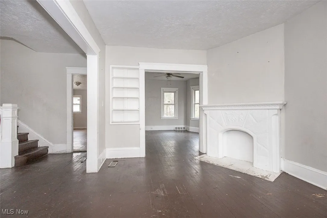 Unfurnished living room with dark wood-style flooring, a textured ceiling, a premium fireplace, built in shelves, and a ceiling fan