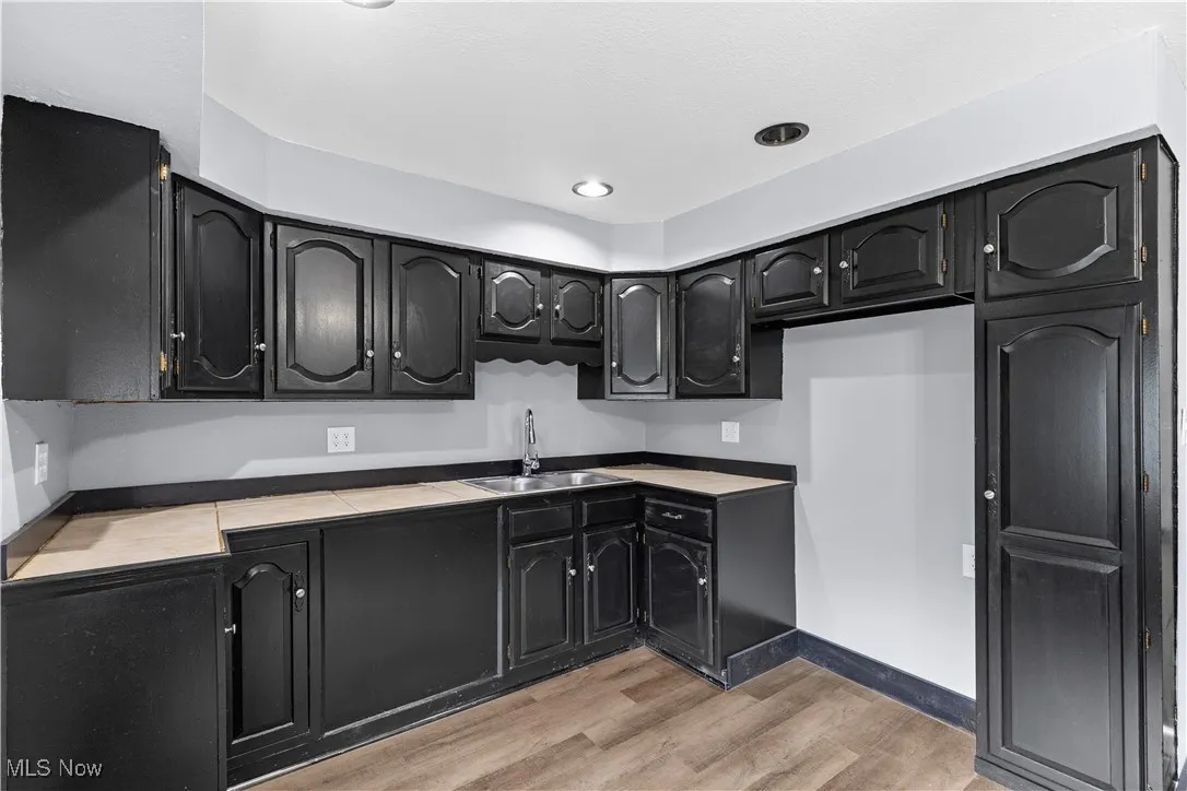 Kitchen with dark cabinetry, light wood-style floors, tile countertops, and recessed lighting
