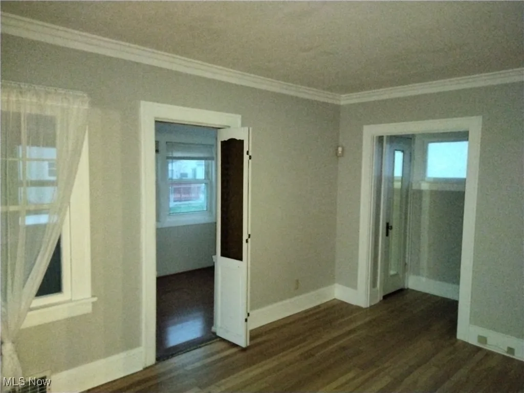 Empty room featuring crown molding and dark wood-type flooring