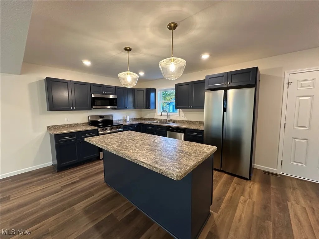 Kitchen featuring appliances with stainless steel finishes, a kitchen island, hanging light fixtures, dark wood-style floors, and recessed lighting