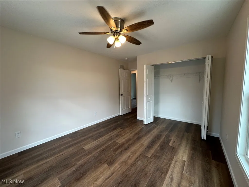 Unfurnished bedroom featuring dark wood-type flooring, a closet, and a ceiling fan