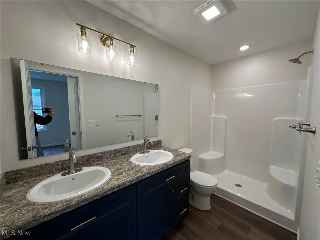 Full bathroom featuring double vanity, dark wood-style floors, a shower, and recessed lighting