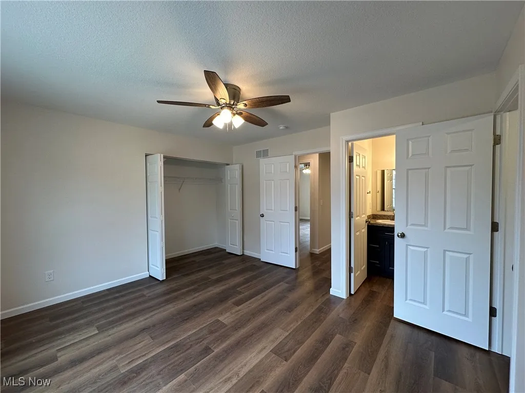 Unfurnished bedroom featuring dark wood-style floors, ensuite bath, ceiling fan, a closet, and a textured ceiling
