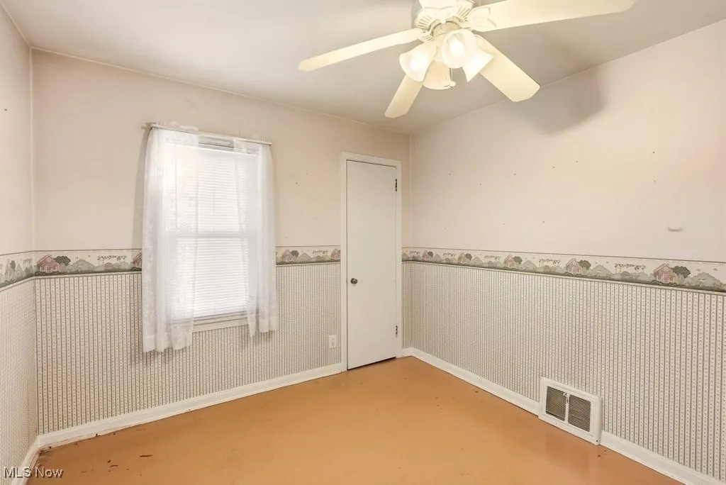 Unfurnished room featuring a wainscoted wall and a ceiling fan