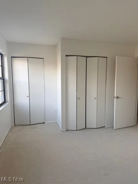 Unfurnished bedroom featuring light colored carpet and multiple closets