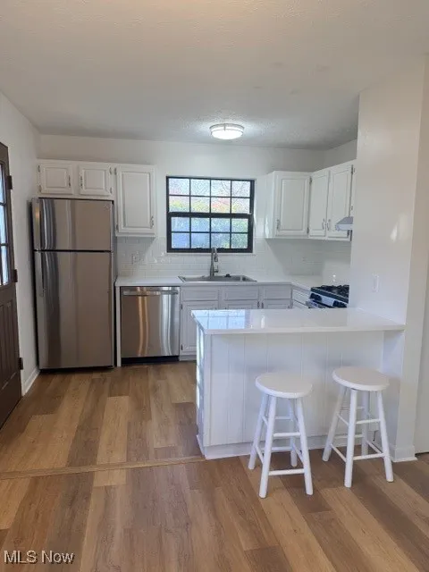 Kitchen with white cabinets, a breakfast bar, refrigerator, decorative backsplash, and light wood-style flooring