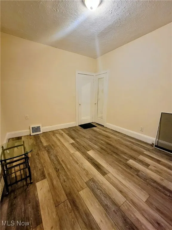Empty room with a textured ceiling and hardwood / wood-style flooring