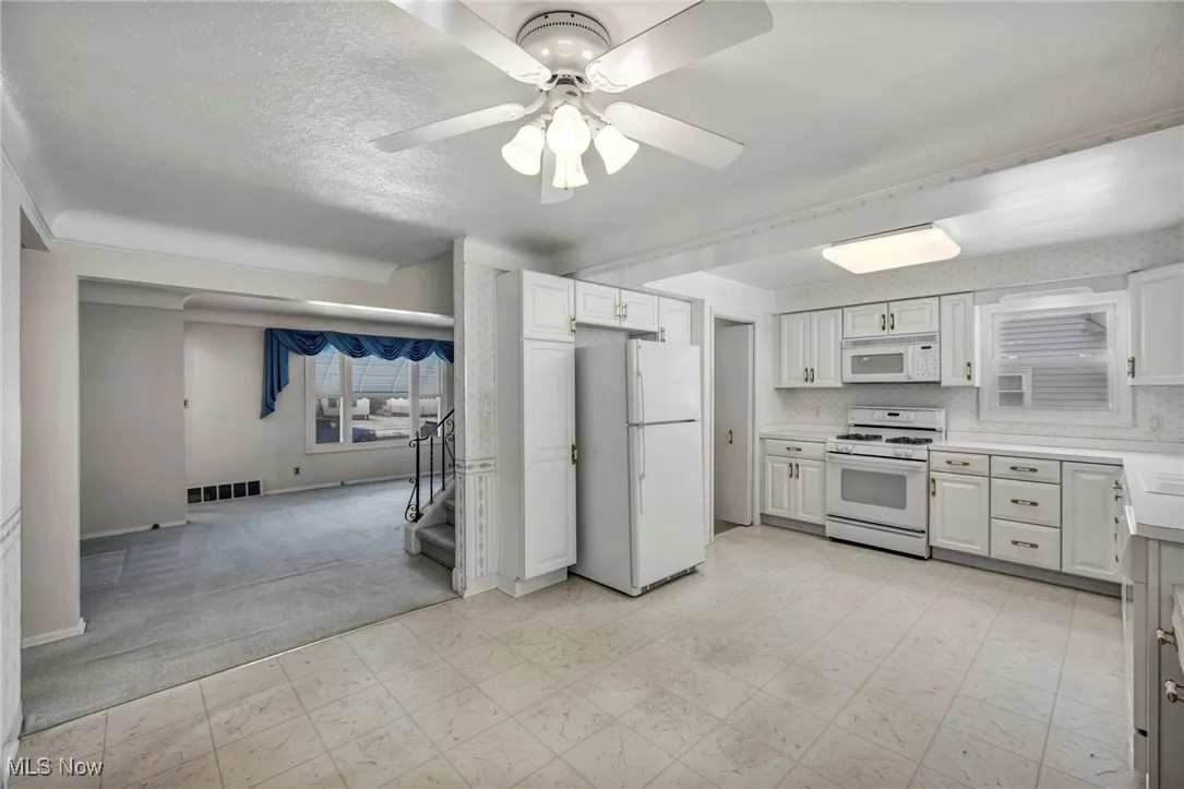 Kitchen with white appliances, light carpet, light countertops, white cabinetry, and light floors