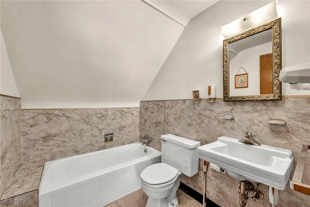 Full bath featuring a bath, vaulted ceiling, tile walls, and a wainscoted wall