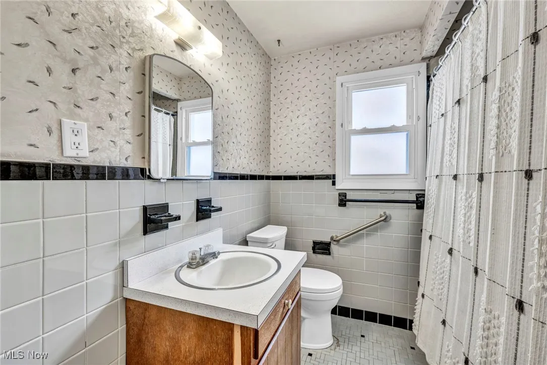 Bathroom featuring tile walls, vanity, a wainscoted wall, light tile patterned floors, and wallpapered walls