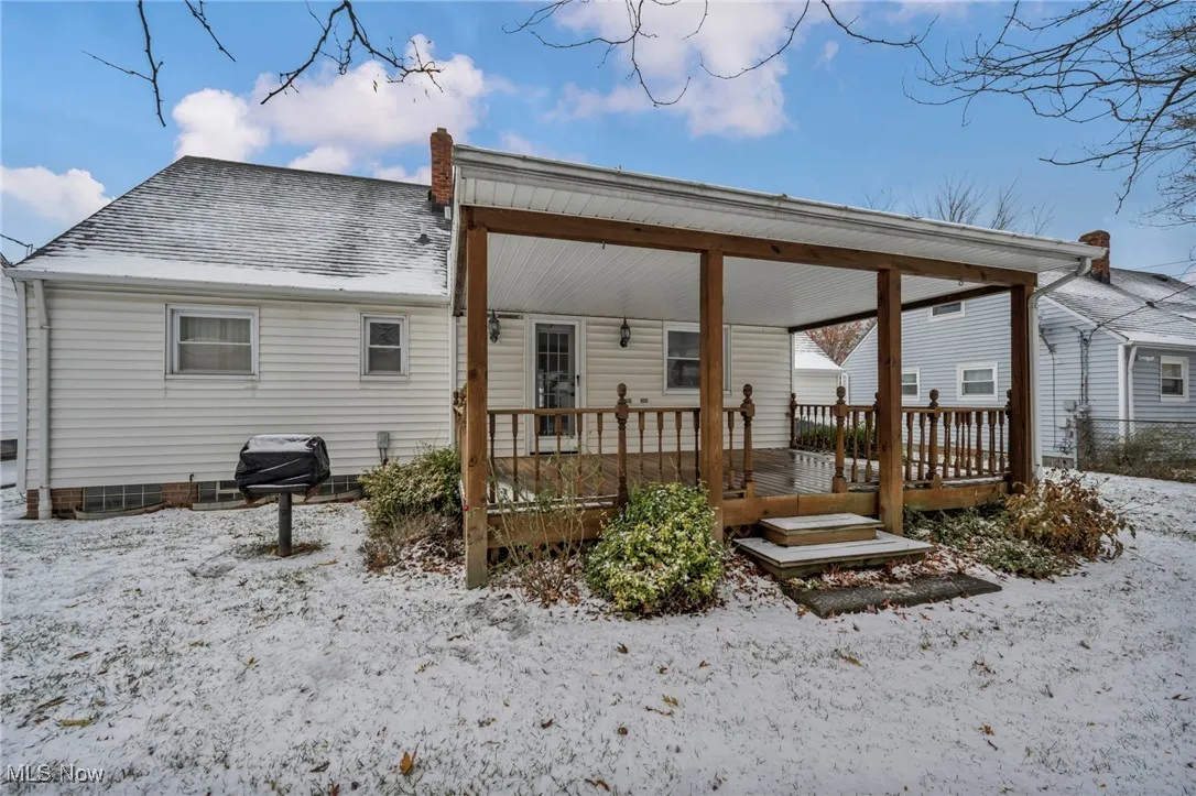Snow covered back of property with a wooden deck and a shingled roof