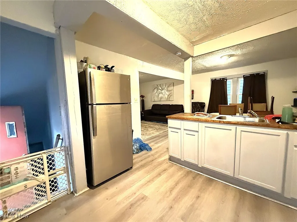 Kitchen featuring a textured ceiling, freestanding refrigerator, white cabinetry, and light wood-style floors