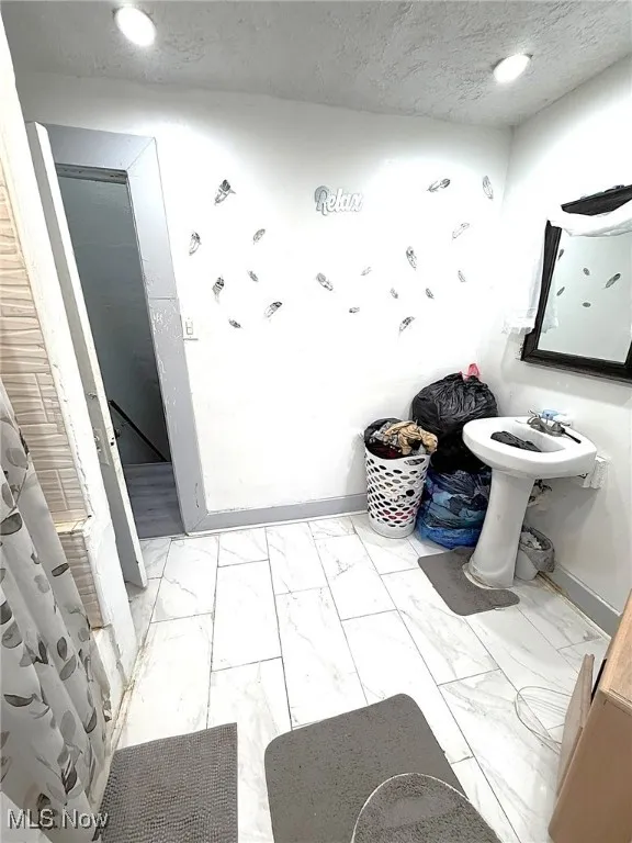 Full bath with a textured ceiling and light marble finish floors