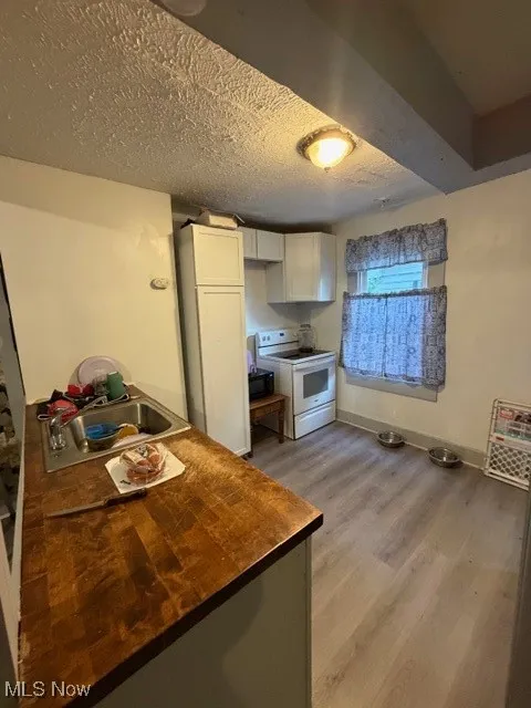 Kitchen with white cabinetry, light wood-style floors, white range oven, wooden counters, and a textured ceiling