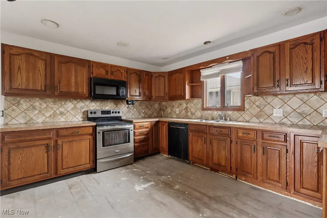 Kitchen with black appliances, brown cabinetry, light countertops, and tasteful backsplash