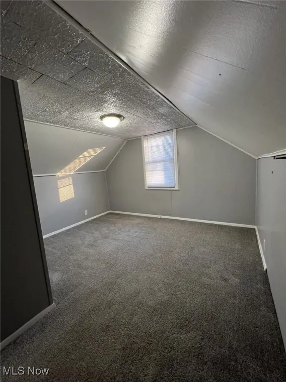 Bonus room with dark colored carpet, a textured ceiling, and vaulted ceiling