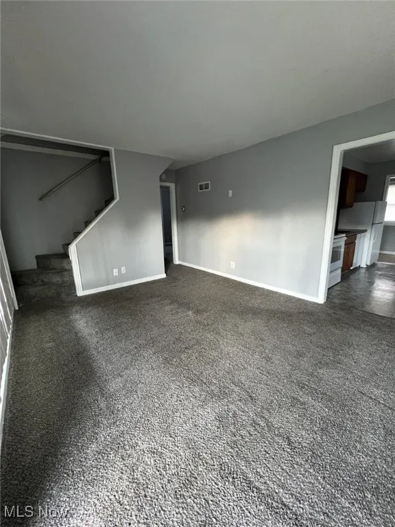 Unfurnished living room featuring baseboards and stairway