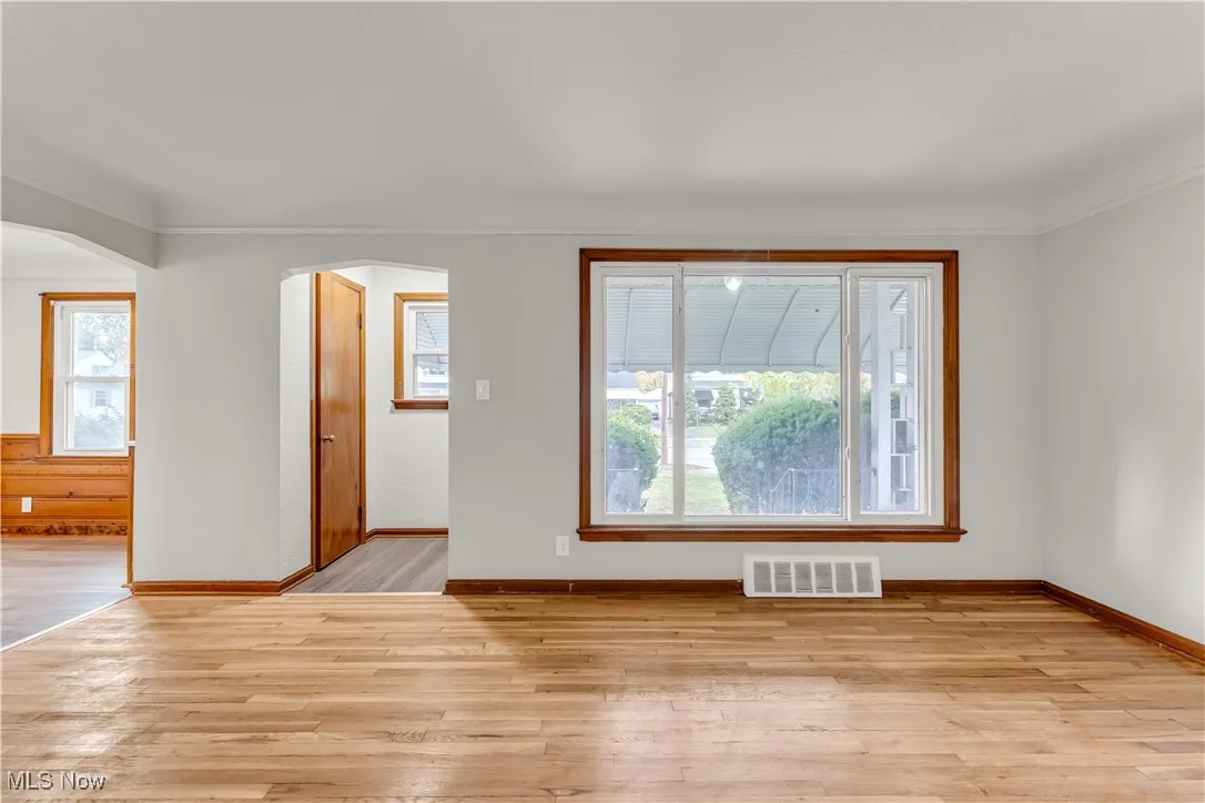 Empty room with light wood-style flooring, plenty of natural light, arched walkways, and crown molding