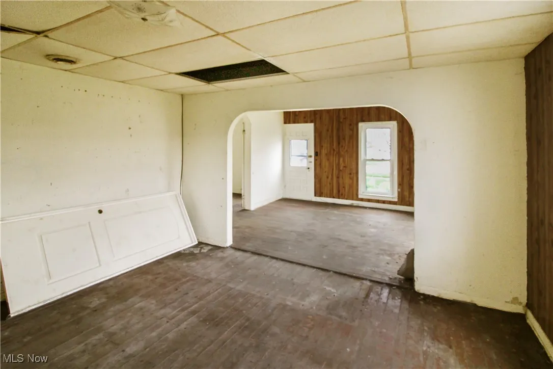 Spare room featuring arched walkways, a drop ceiling, and dark wood-style floors
