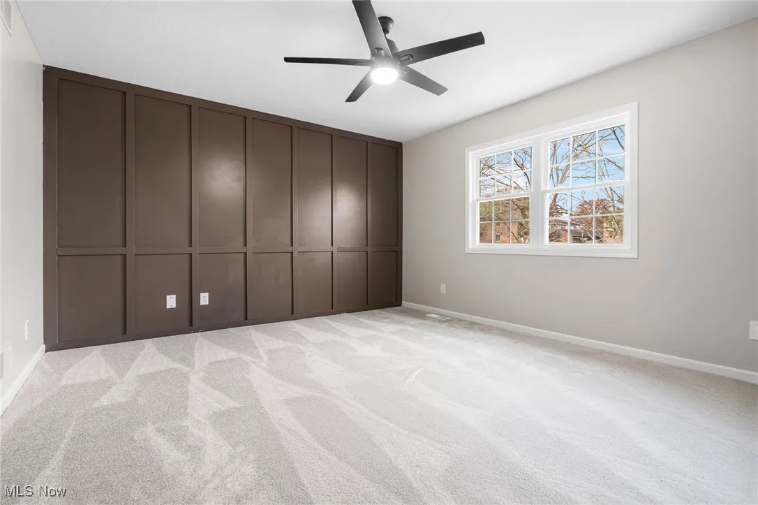Unfurnished bedroom with a decorative wall, light colored carpet, a ceiling fan, and a closet