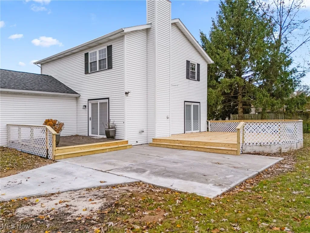 Back of property with a deck, a shingled roof, a chimney, and a patio