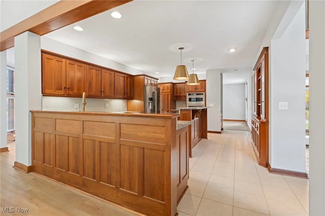 Kitchen featuring brown cabinets, a peninsula, recessed lighting, hanging light fixtures, and backsplash