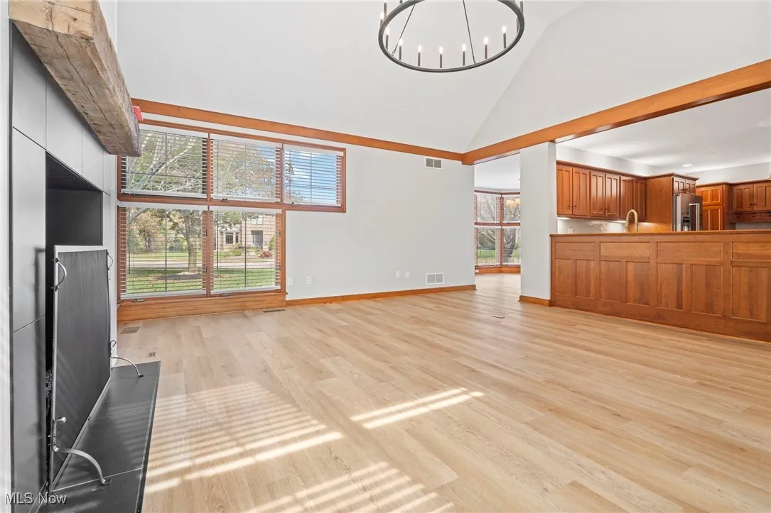 Unfurnished living room featuring light wood-type flooring, high vaulted ceiling, and a chandelier