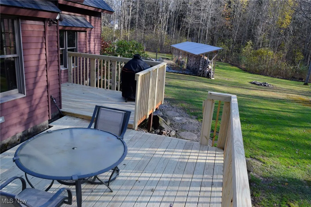 Deck with a yard, outdoor dining space, a grill, and a wooded view