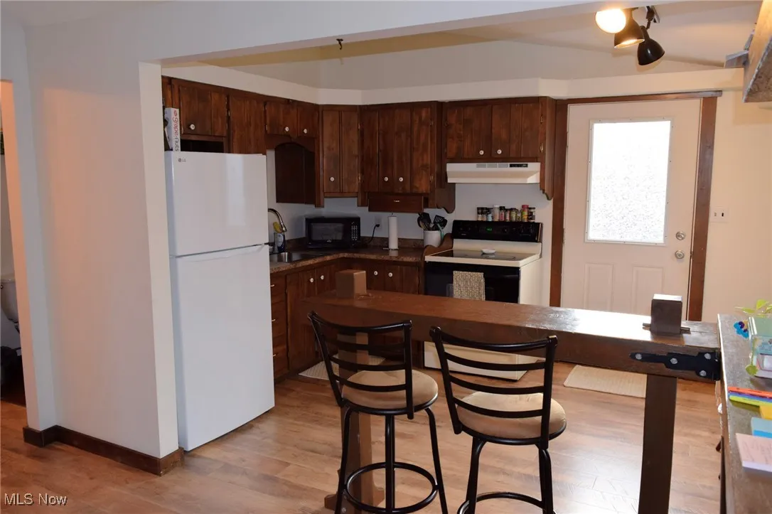 Kitchen in the apartment featuring freestanding refrigerator, dark brown cabinetry, range with electric stovetop, dark countertops, and light wood-type flooring