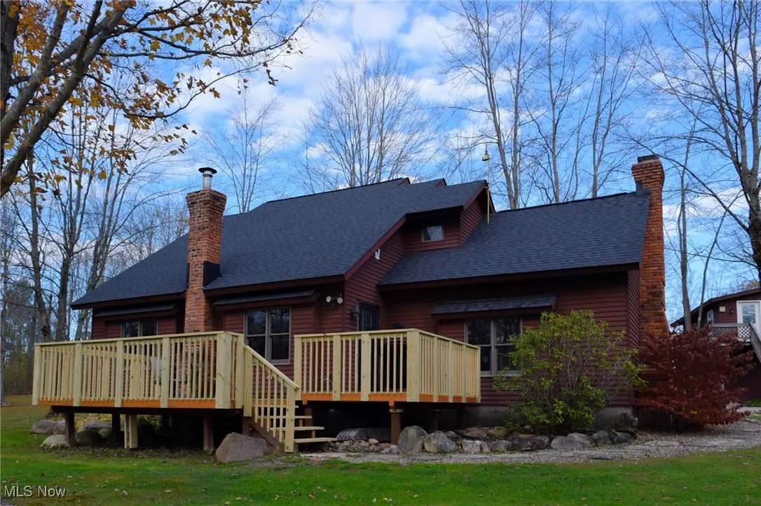 Rear view of house featuring a wooden deck, a chimney, a shingled roof, and a lawn