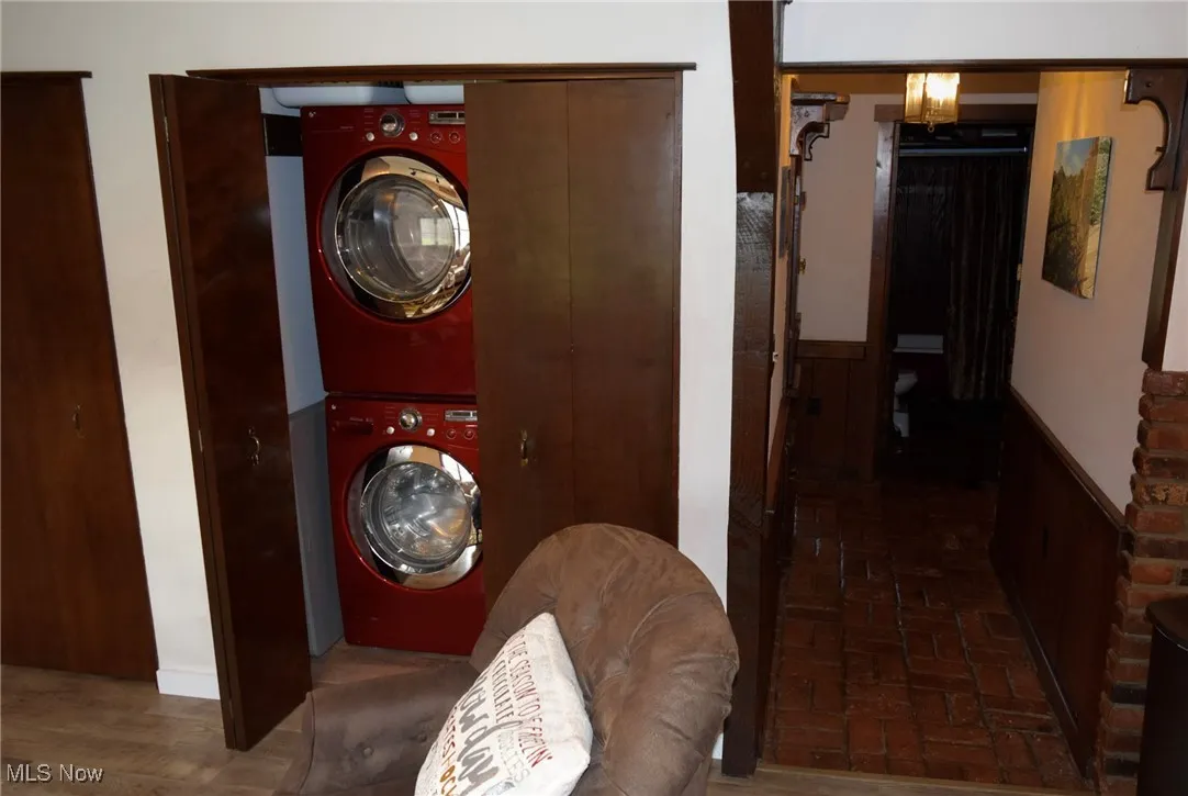 Laundry area featuring a wainscoted wall, stacked washer / drying machine, and brick patterned floors