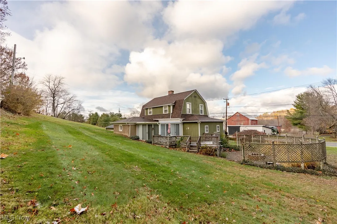 Back of property featuring a gambrel roof, a chimney, a yard, and a wooden deck