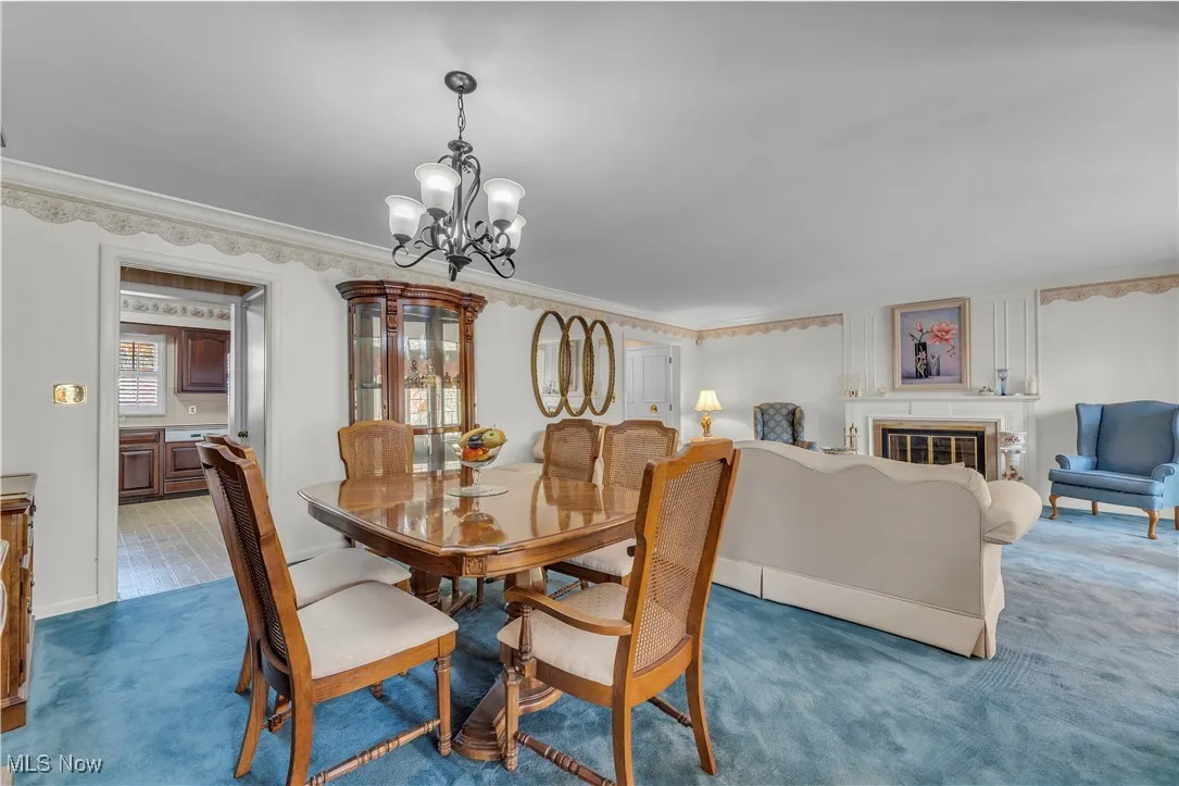 Dining area featuring carpet, a chandelier, a glass covered fireplace, and crown molding