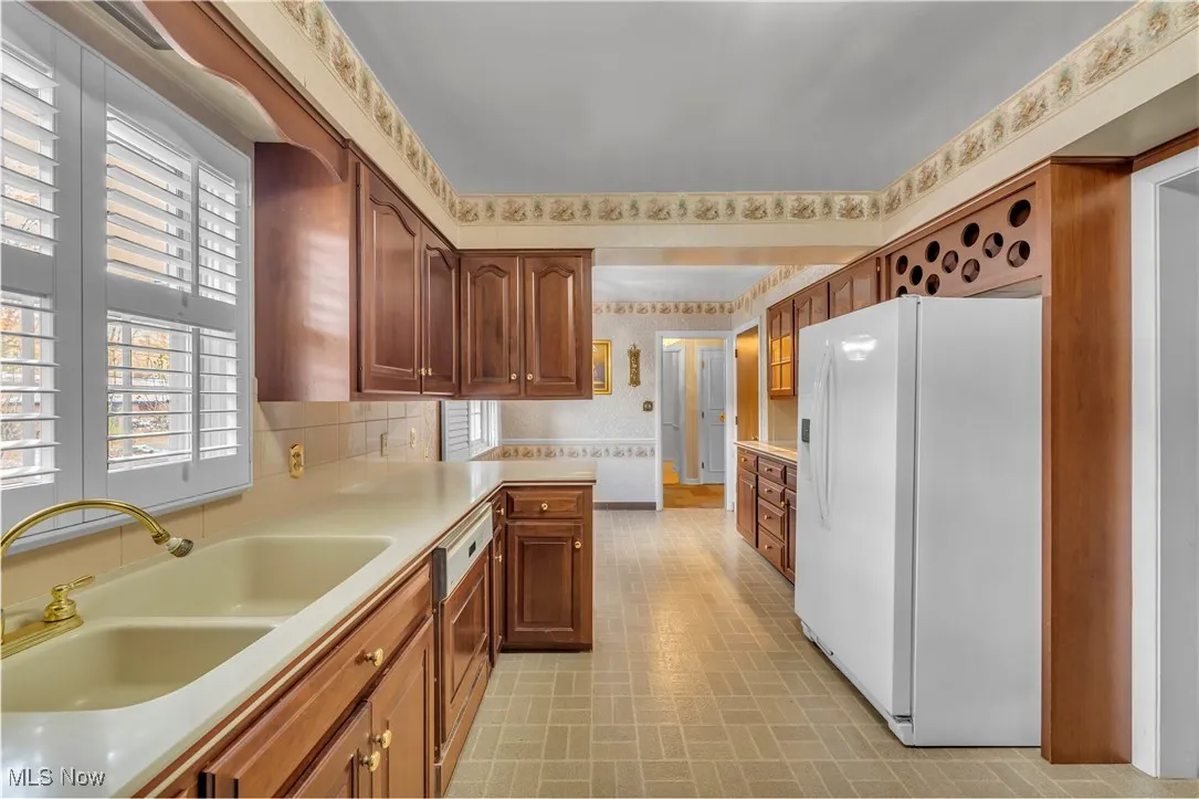 Kitchen with wallpapered walls, white fridge with ice dispenser, light countertops, brick patterned flooring, and dishwasher