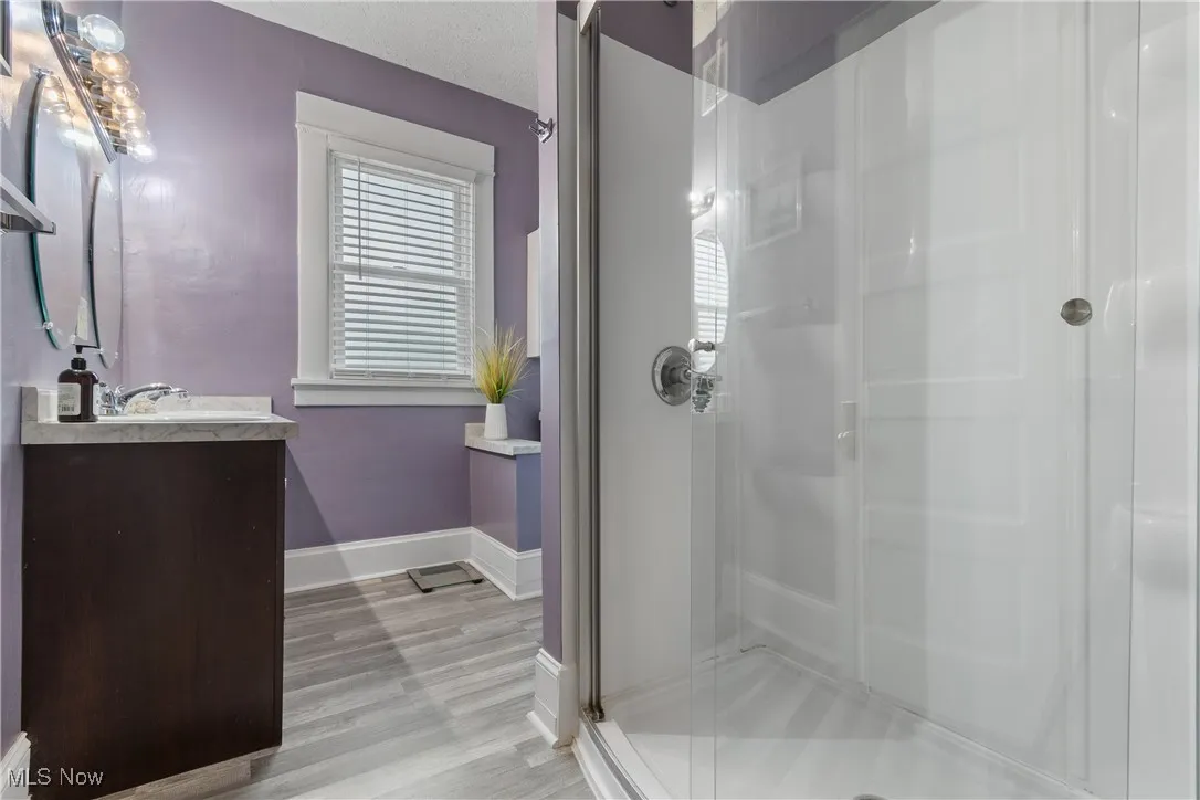 Full bathroom featuring vanity, a stall shower, light wood-type flooring, and a textured ceiling