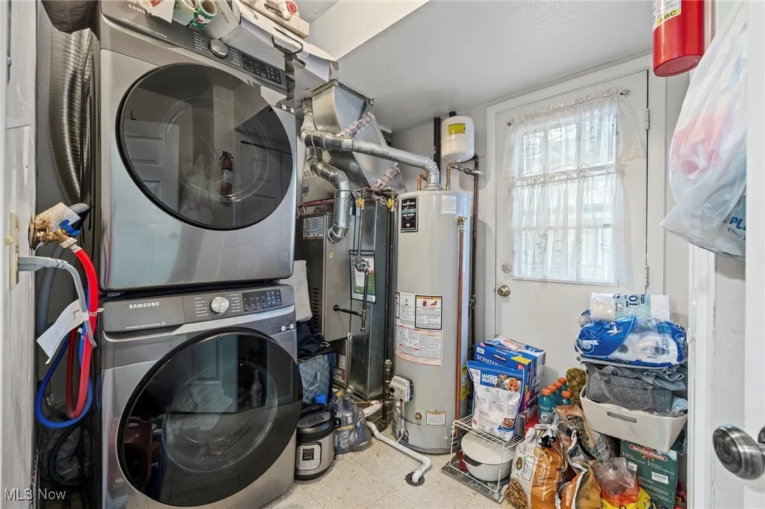 Laundry area featuring stacked washer / drying machine, gas water heater, and heating unit