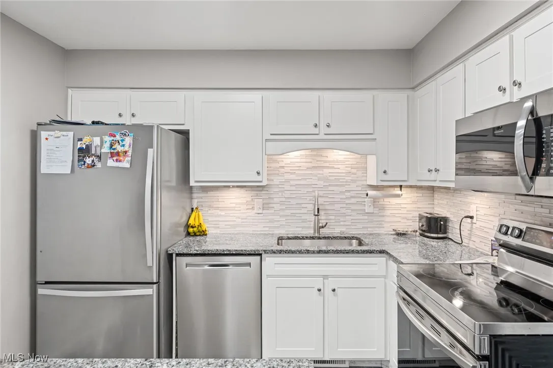 Kitchen with stainless steel appliances, white cabinetry, backsplash, and light stone countertops