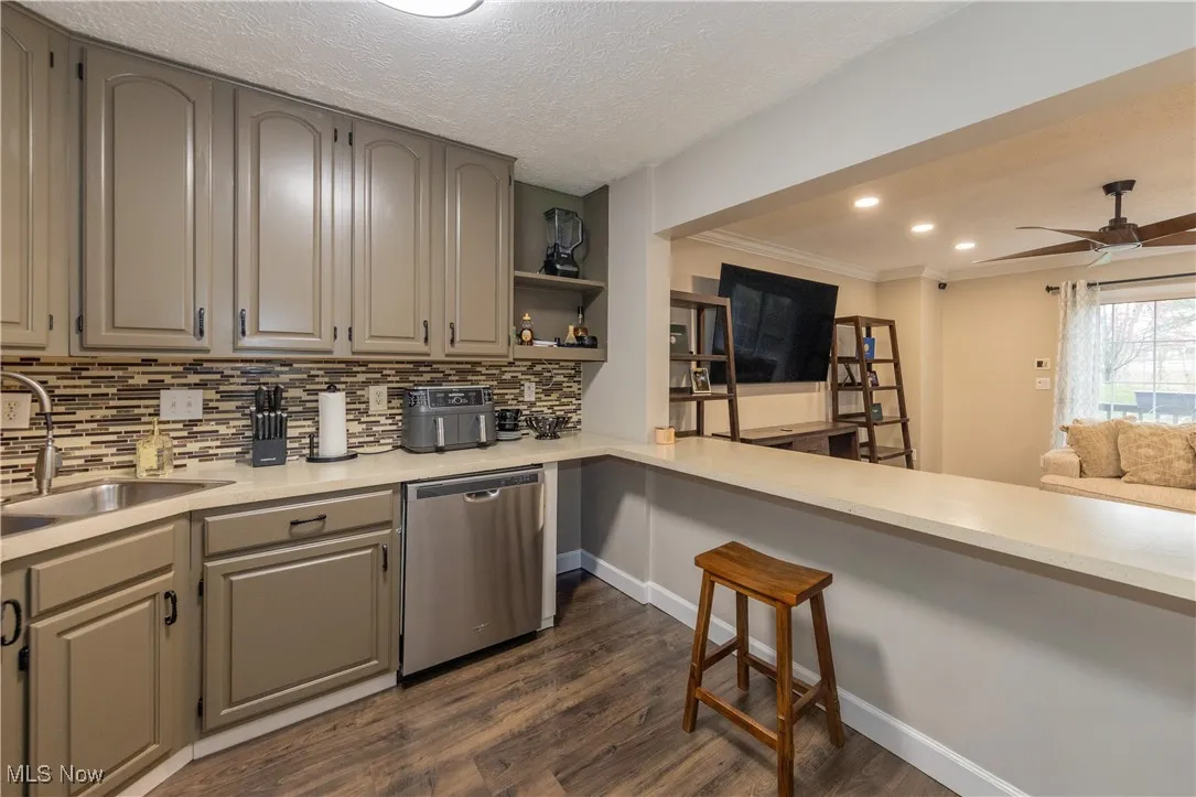 Kitchen featuring dishwasher, dark wood finished floors, a ceiling fan, a breakfast bar area, and recessed lighting