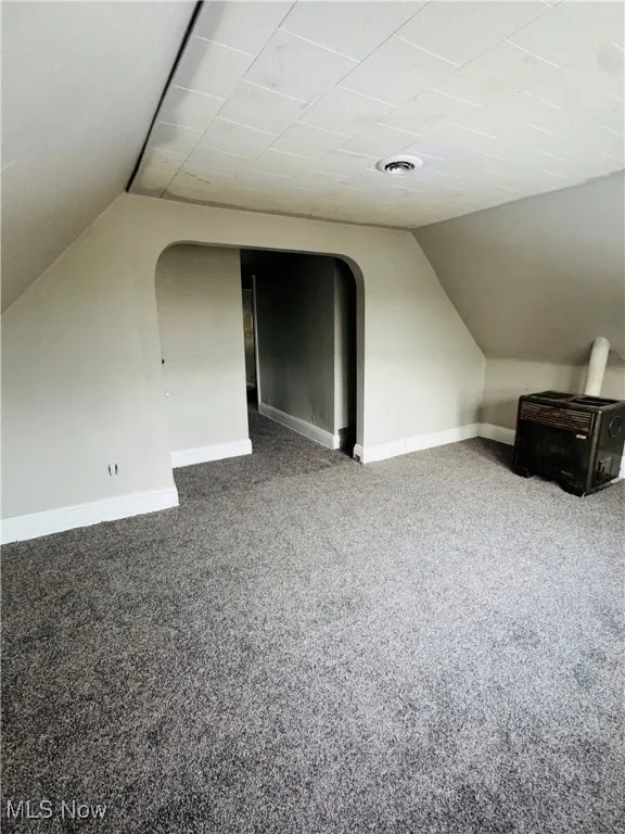 Bonus room with vaulted ceiling, light colored carpet, and arched walkways
