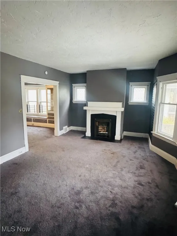 Unfurnished living room with a fireplace with flush hearth, plenty of natural light, carpet, and a textured ceiling