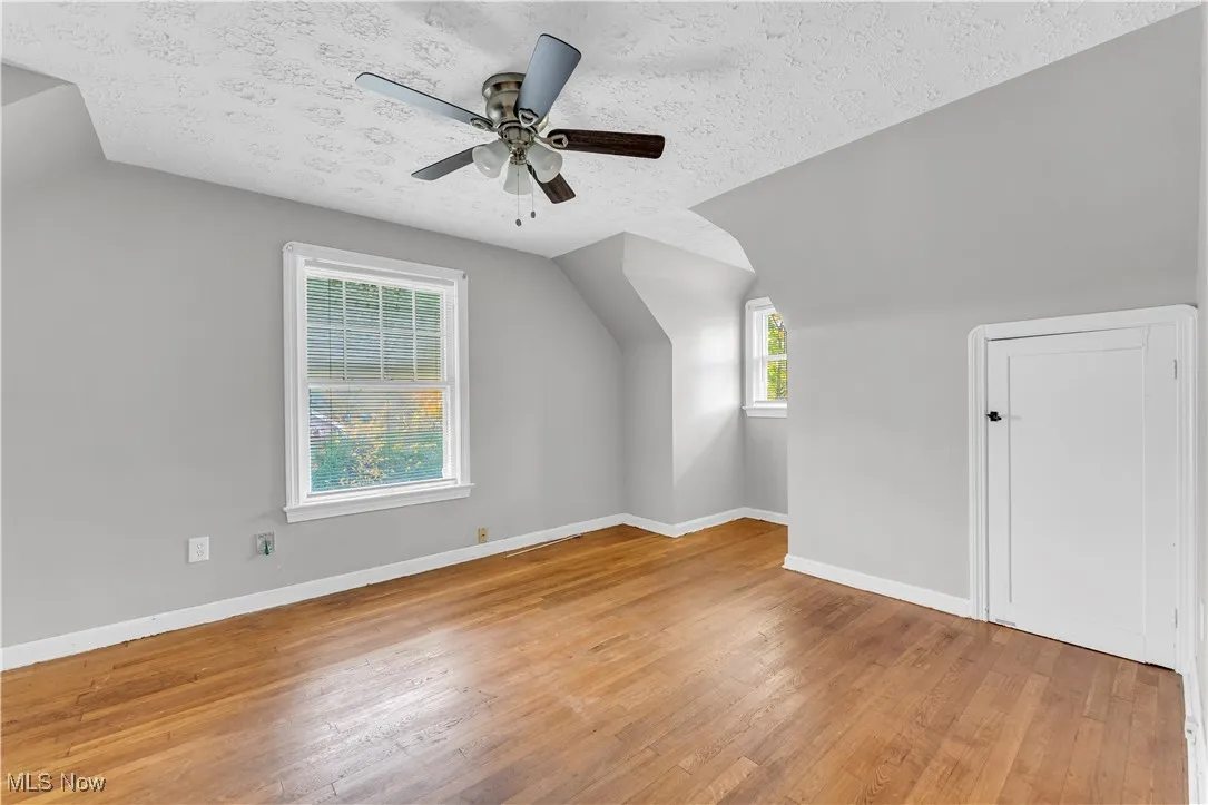Additional living space with a textured ceiling, lofted ceiling, light wood-style flooring, and a ceiling fan