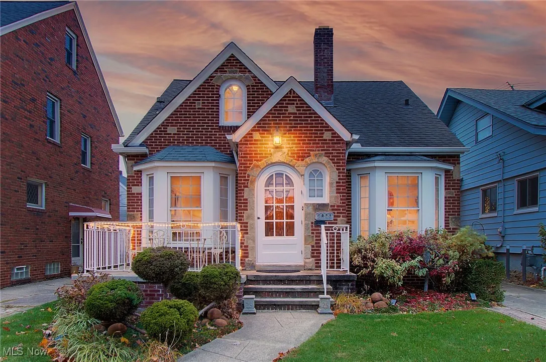 View of front facade with a shingled roof, a chimney, brick siding, and a front lawn