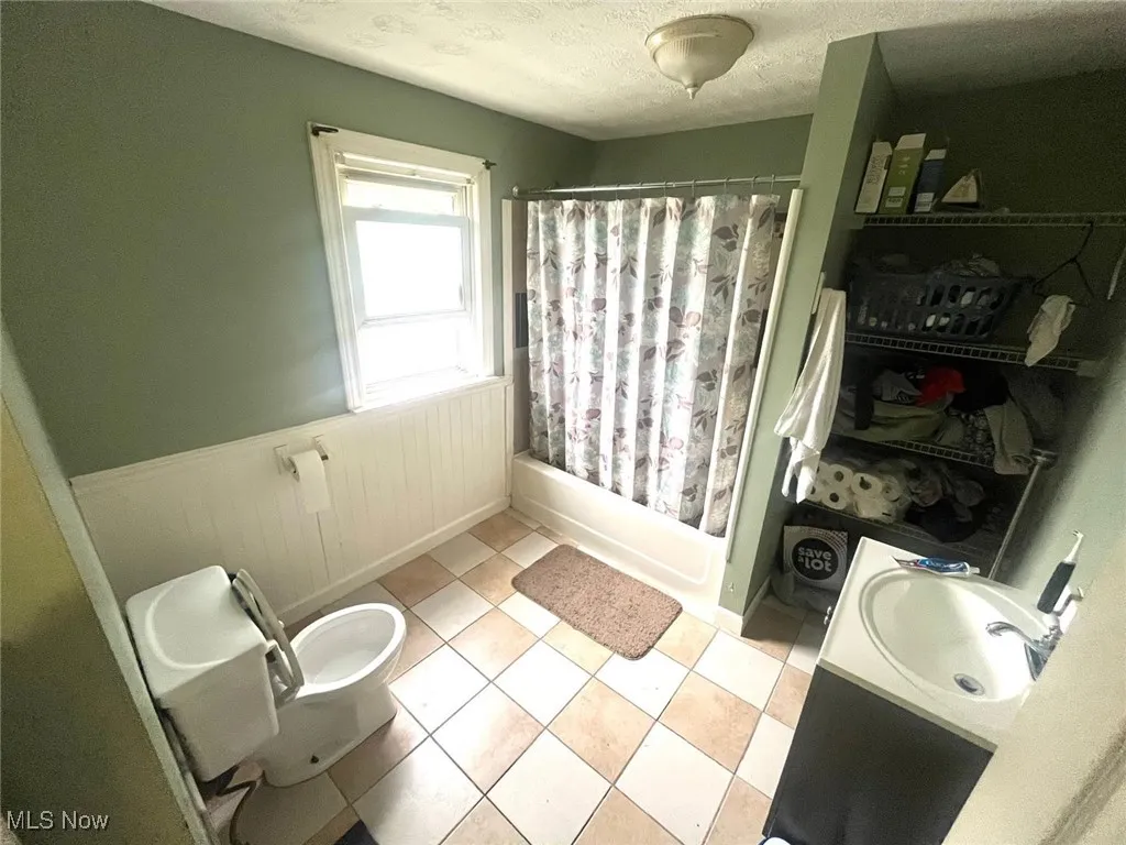 Full bathroom with vanity, a wainscoted wall, shower / tub combo, a textured ceiling, and light tile patterned floors