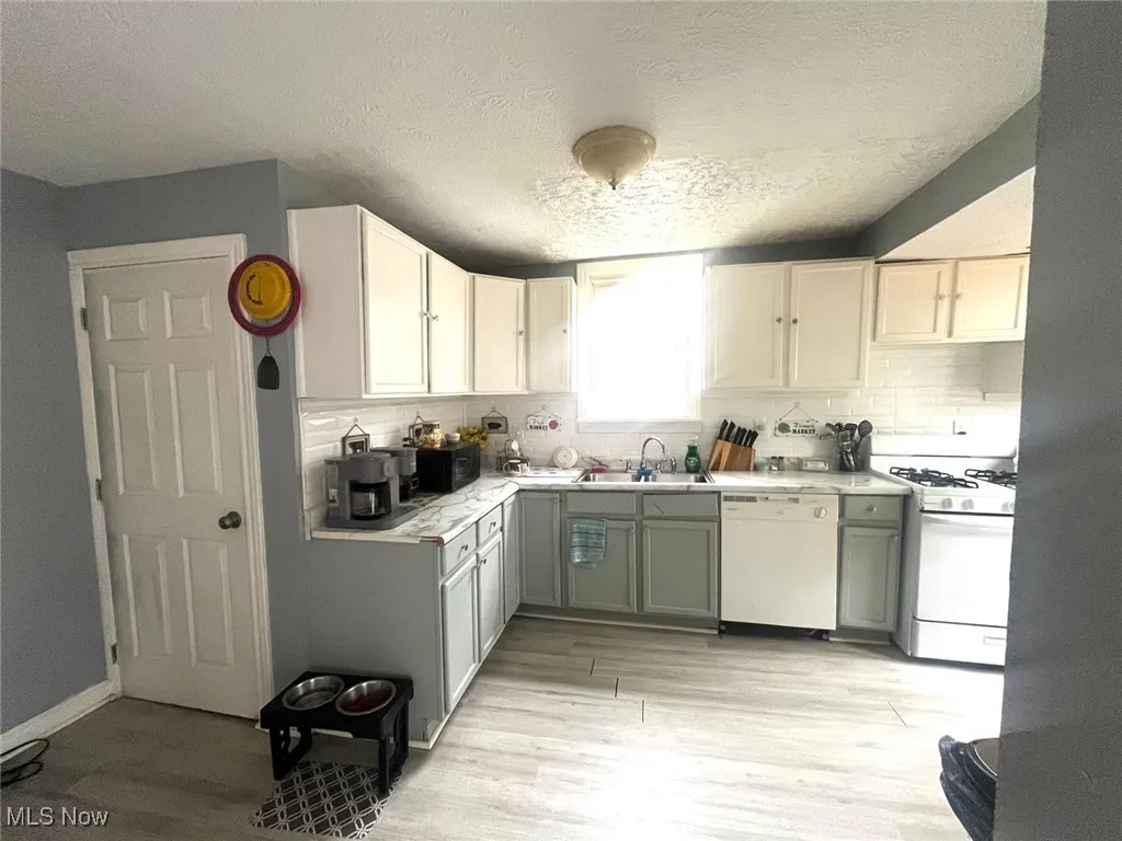 Kitchen featuring light countertops, a textured ceiling, light wood-type flooring, white appliances, and white cabinetry
