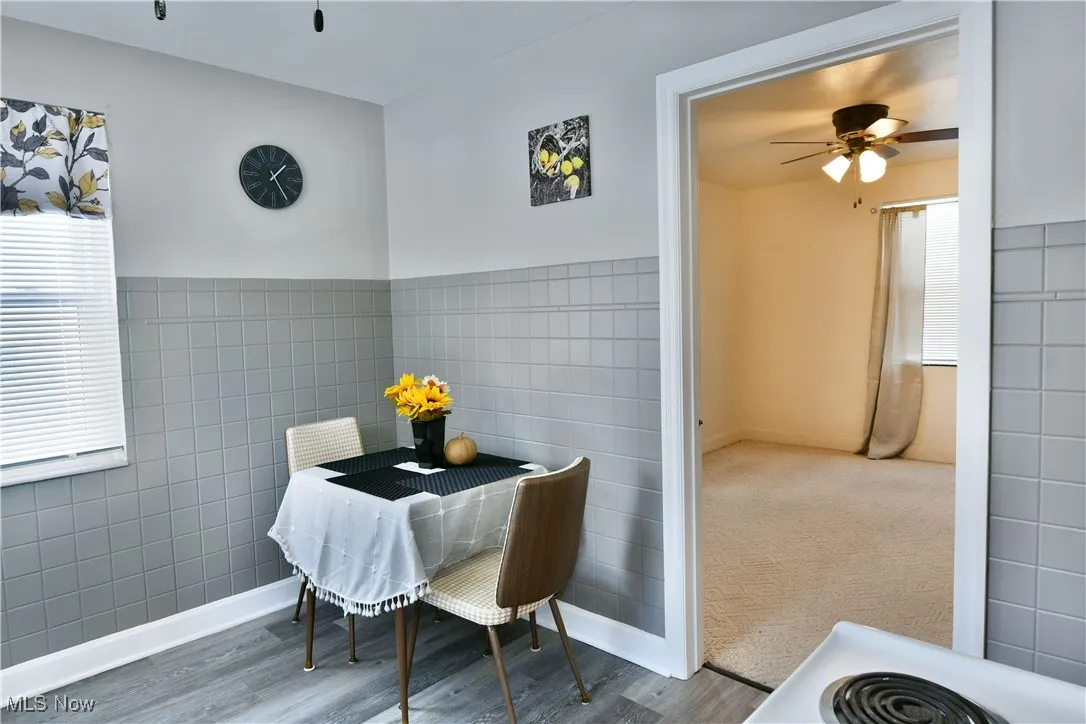 Dining room featuring wood finished floors, tile walls, and ceiling fan