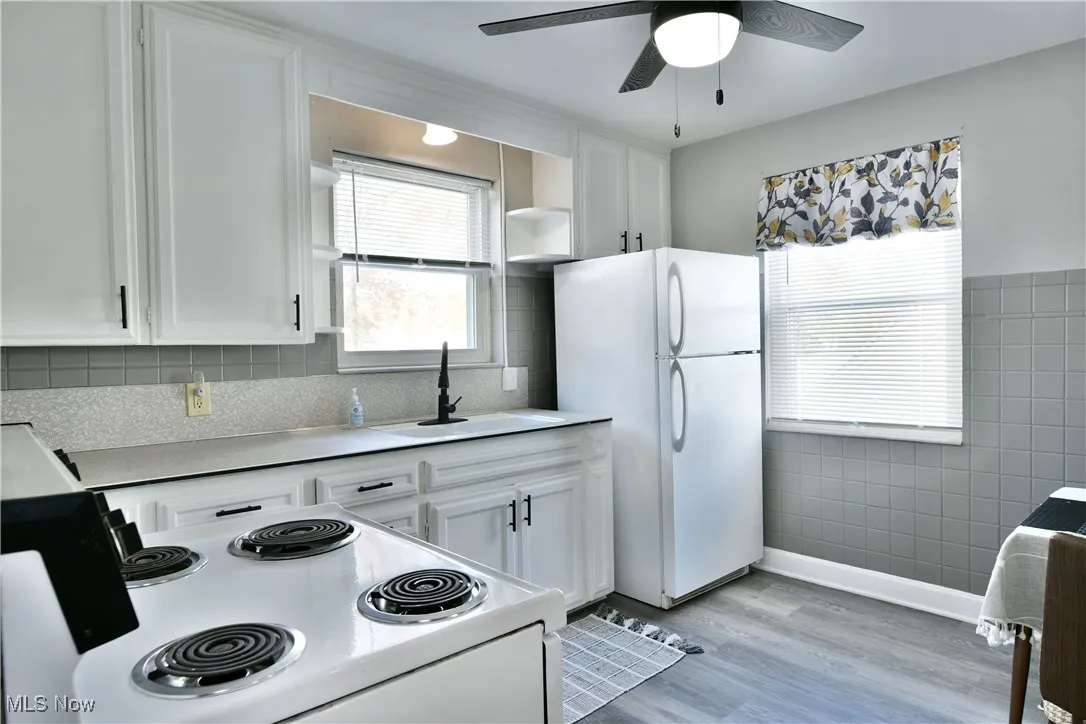 Kitchen with white appliances, white cabinets, light countertops, light wood-style flooring, and healthy amount of natural light