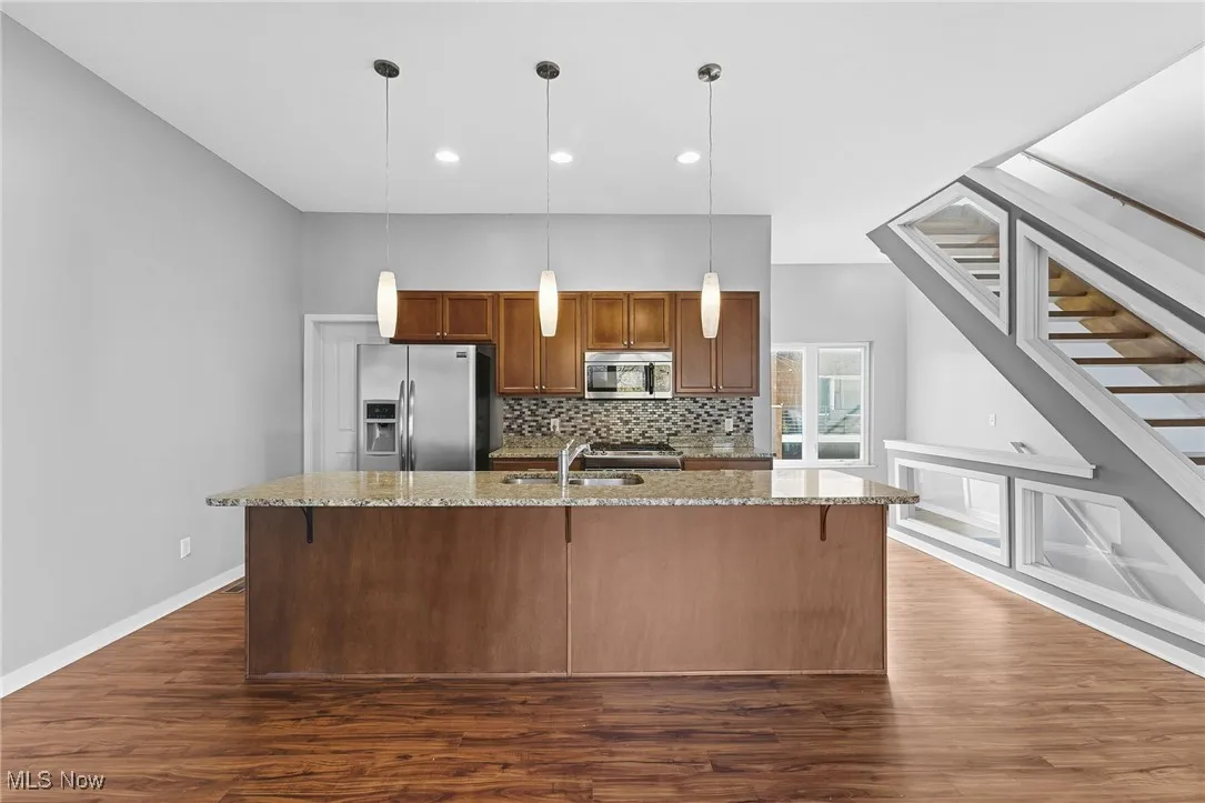 Kitchen featuring light stone counters, brown cabinetry, backsplash, decorative light fixtures, and recessed lighting