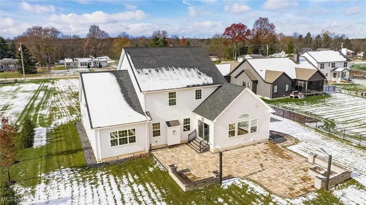 Snow covered back of property featuring a patio area, a residential view, roof with shingles, and entry steps